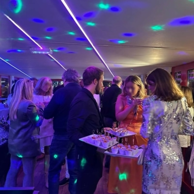 Paris en Bateau - Des personnes en tenue de soirée se mêlent et dégustent des amuse-gueules lors d'une fête en intérieur avec des néons violets et des projections colorées au plafond - un exemple parfait de privatisation de péniche pour différents événements.