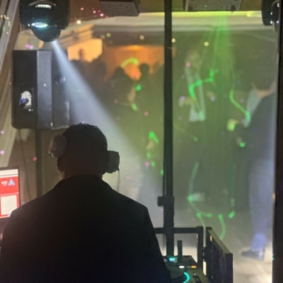 Paris en Bateau - Un DJ portant des écouteurs se tient à une cabine avec des platines, face à une piste de danse avec des lumières colorées et des gens qui dansent en arrière-plan lors d'une privatisation de péniche pour différents événements.
